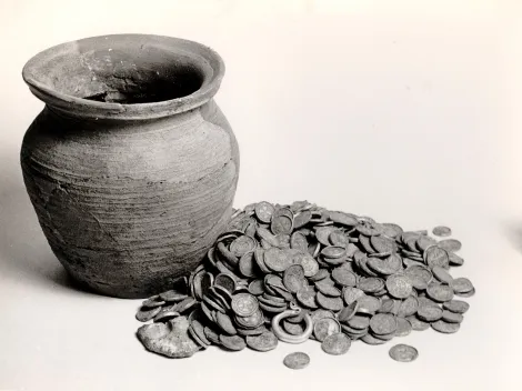 Na zdjęciu widoczne jest naczynie gliniane, obok którego rozsypany jest stos monet oraz kabłączek skroniowy. Skarb pochodzi z Leźnicy Małej w województwie łódzkim, ukryty został na początku XII wieku.