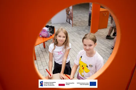 Dwie dziewczynki w wieku szkolnym trzymające kartki oraz pisaki podczas zajęć towarzyszących otwarciu wystawy. 