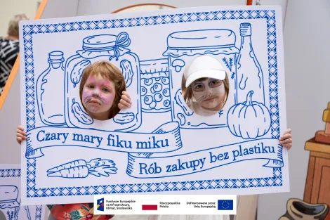 Dwie dziewczynki z pomalowanymi twarzami w monidle stylizowanym na starodawną makatkę z napisem „fiku miku, rób zakupy bez plastiku”