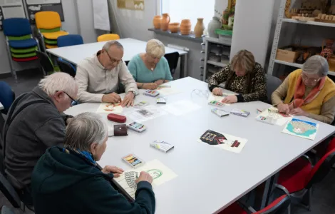 Sześcioro starszych ludzi siedzi przy stole. Wszyscy kolorują obrazki.