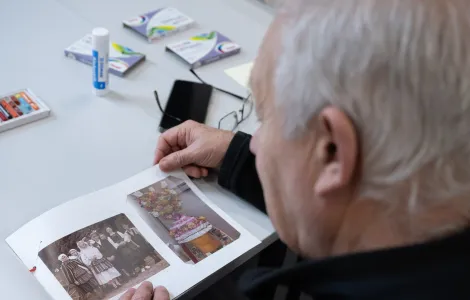 Starszy mężczyzna siedzi przy stole i ogląda album ze starymi zdjęciami.